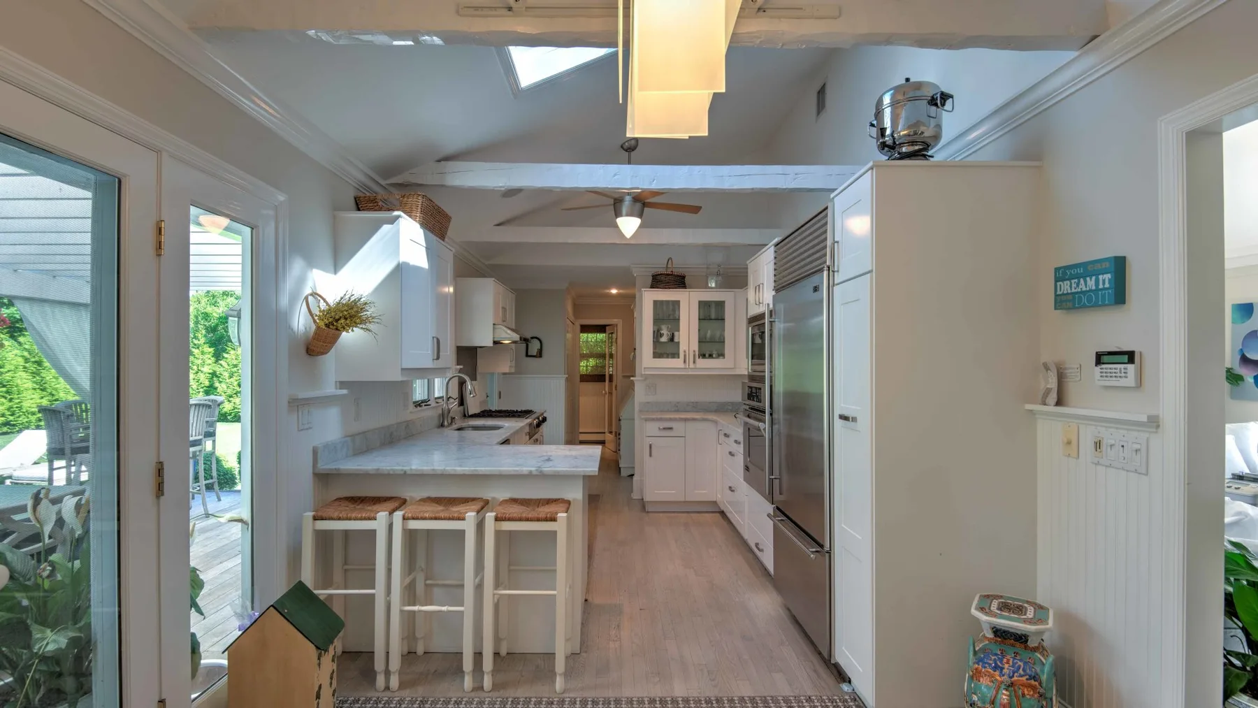 A bright kitchen with a central island, cabinetry, and glass doors opening to greenery.
