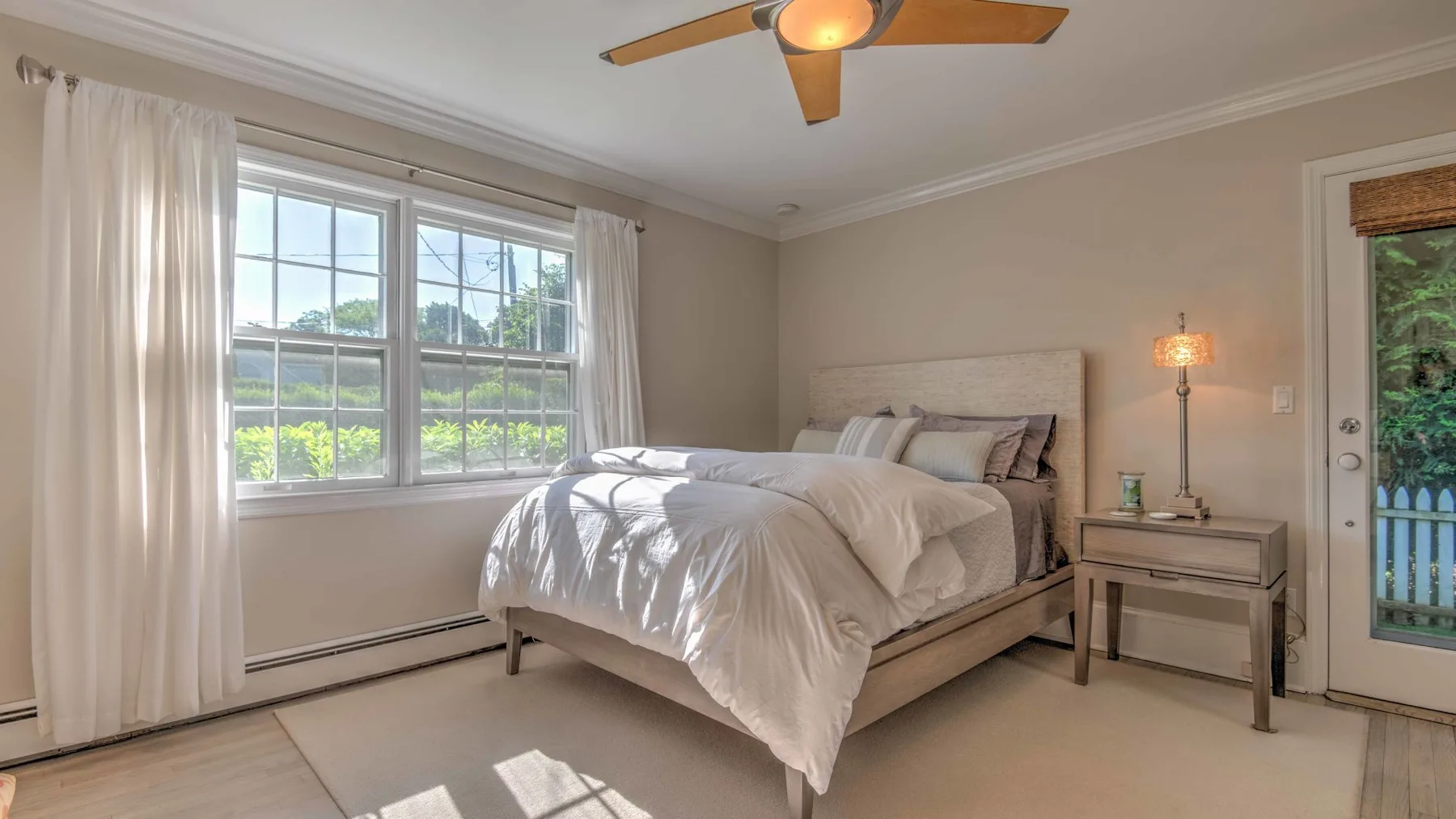 A bright bedroom with a bed beside large windows and a small bedside table.