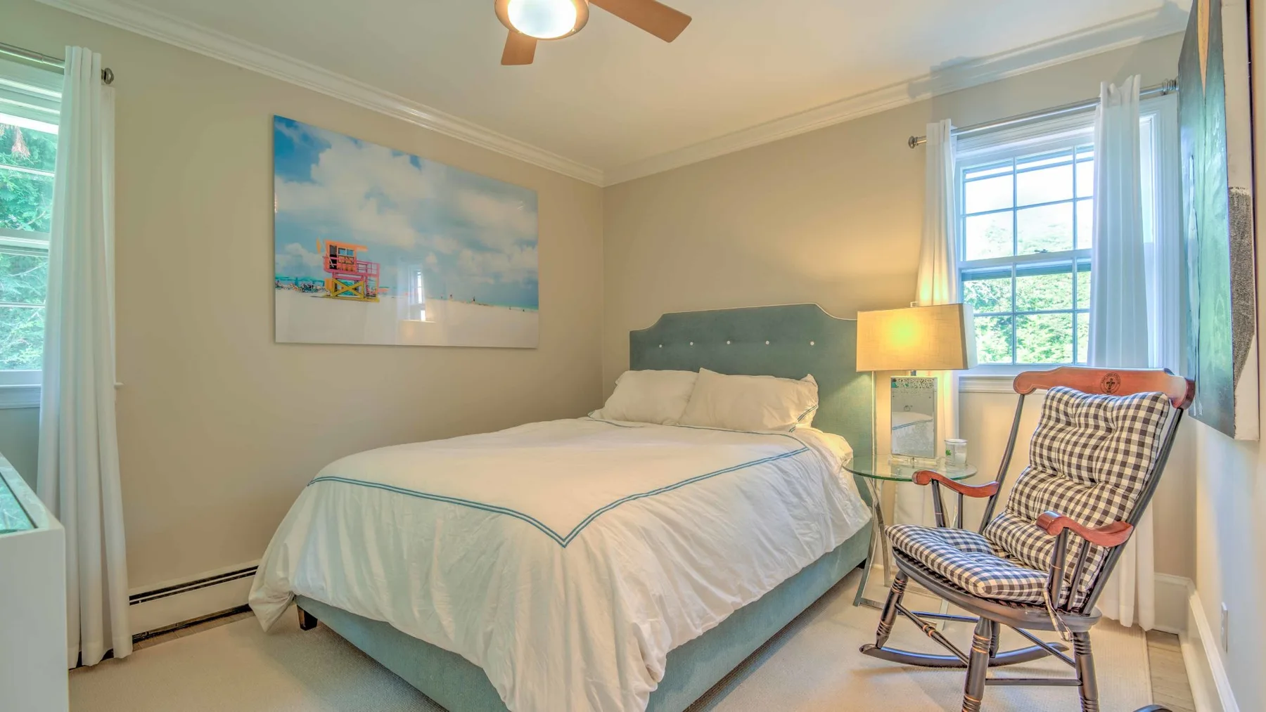 A bedroom with a bed, framed wall art, and a chair beside the window.