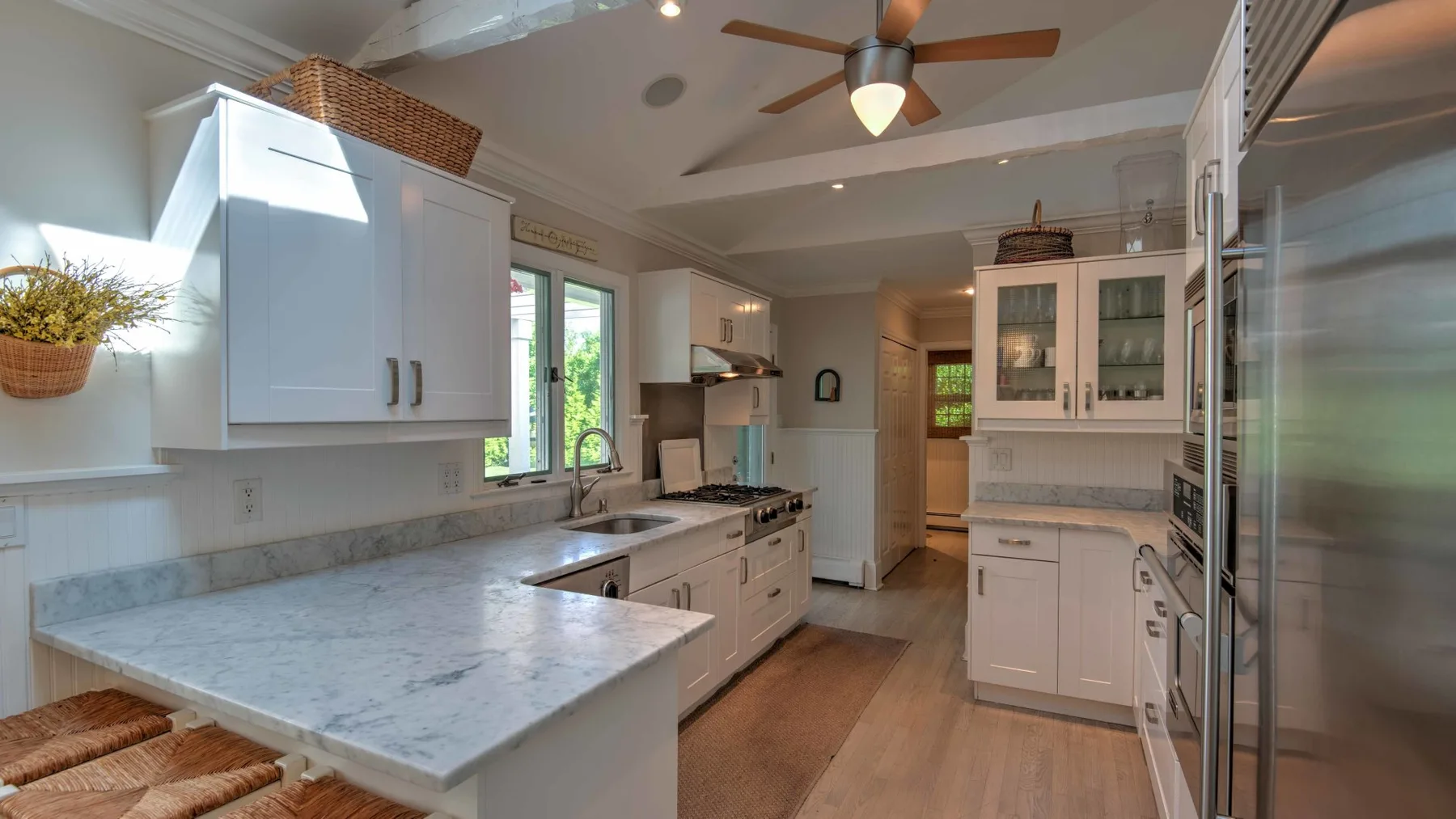 A bright kitchen with white cabinets, stone countertops, and a ceiling fan.
