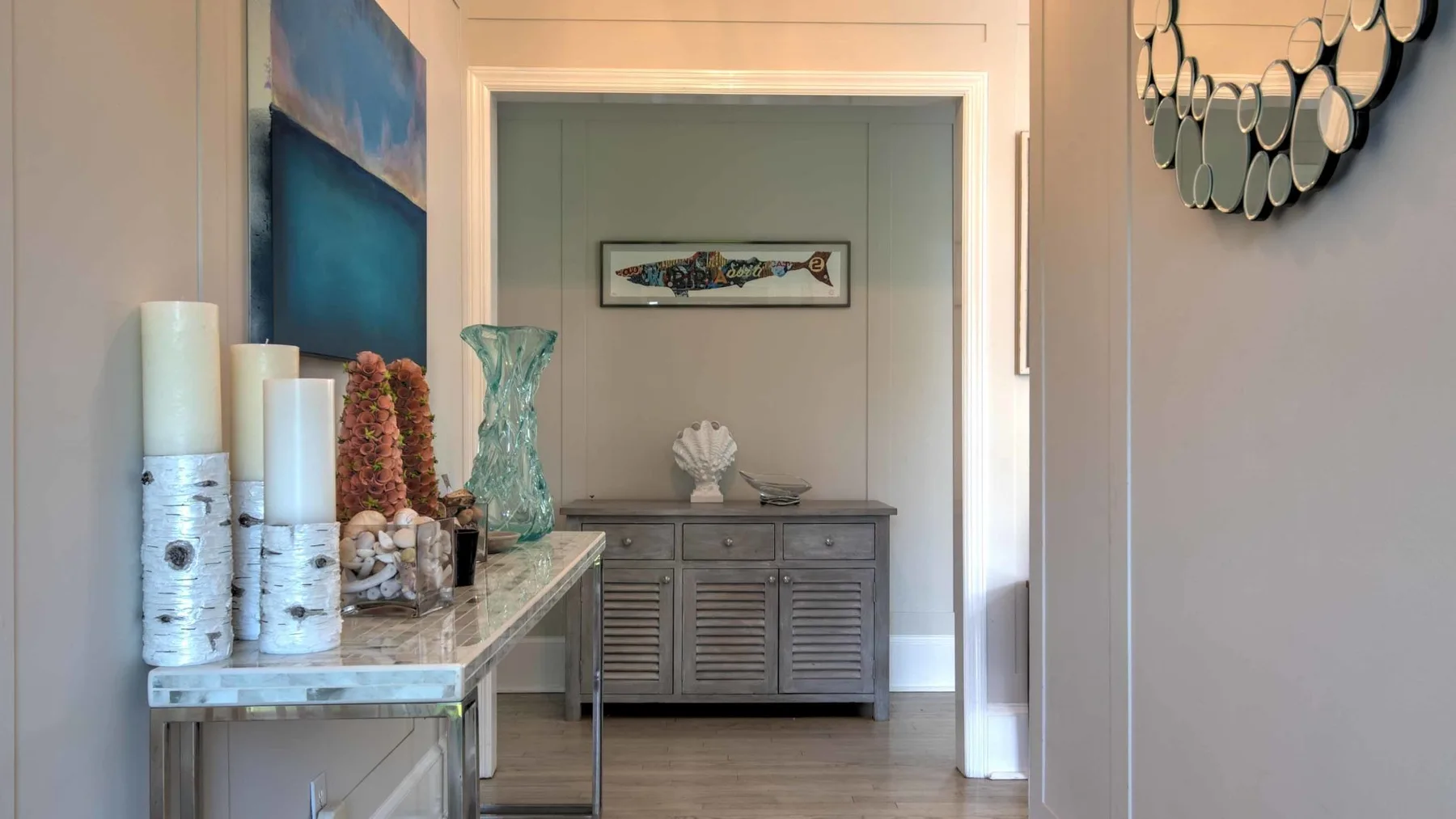 A hallway displays a console table, decorative objects, and framed artwork.