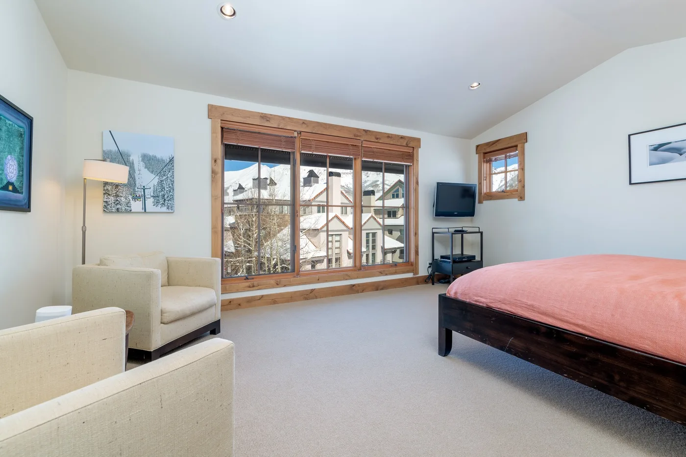 A bedroom with a bed, seating, and a large window overlooking neighboring buildings.