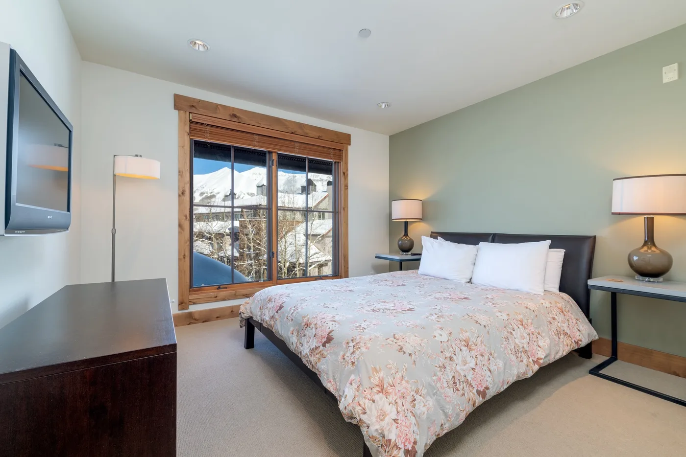 A bedroom with a bed beside a large window overlooking snowy mountains.