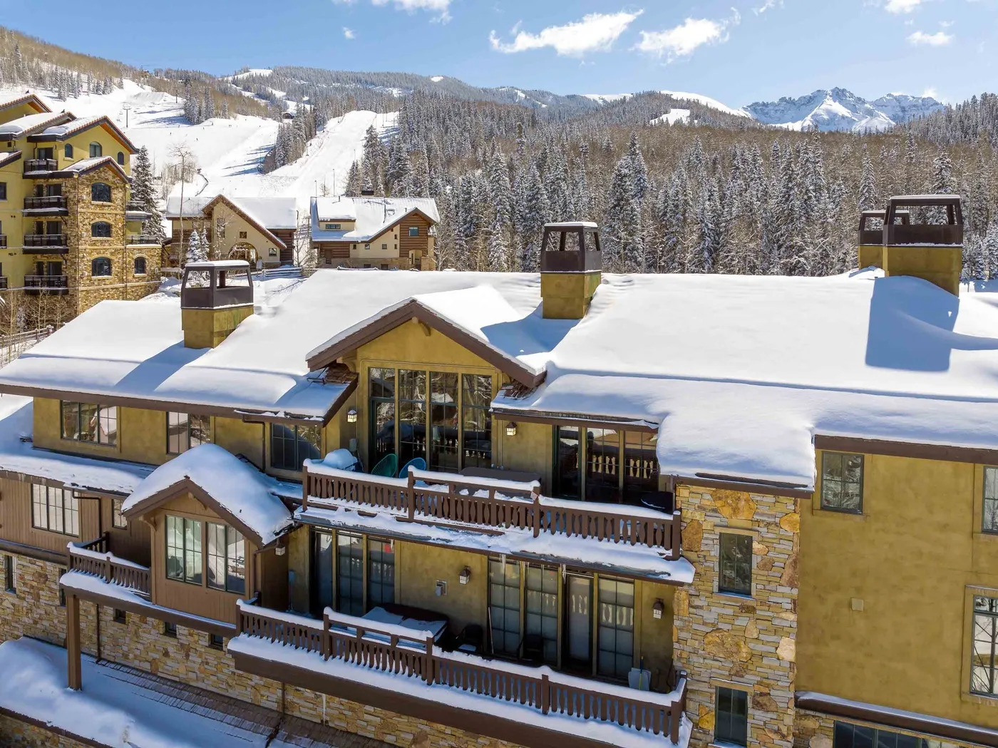 A snow-covered mountain lodge overlooks a forested, snowy mountain landscape.