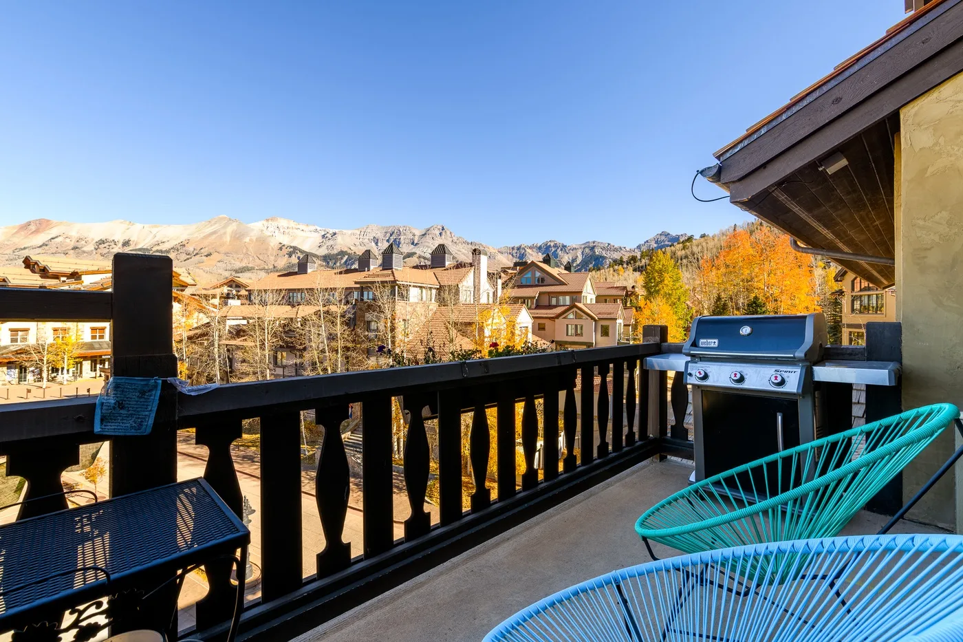 A balcony seating area overlooks nearby buildings and mountain scenery.
