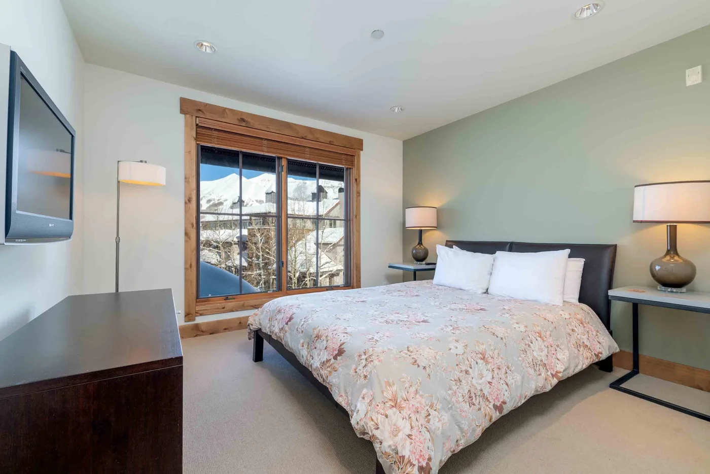 A bedroom with a bed beside a large window overlooking a snowy landscape.