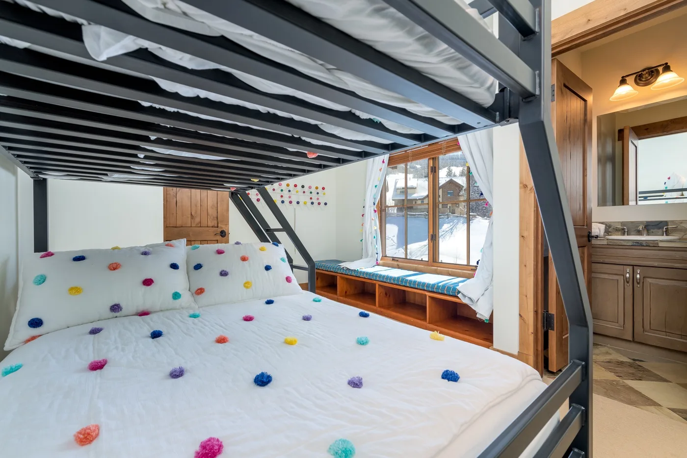 A bedroom with a colorful bed beneath a raised sleeping platform and a window seat.