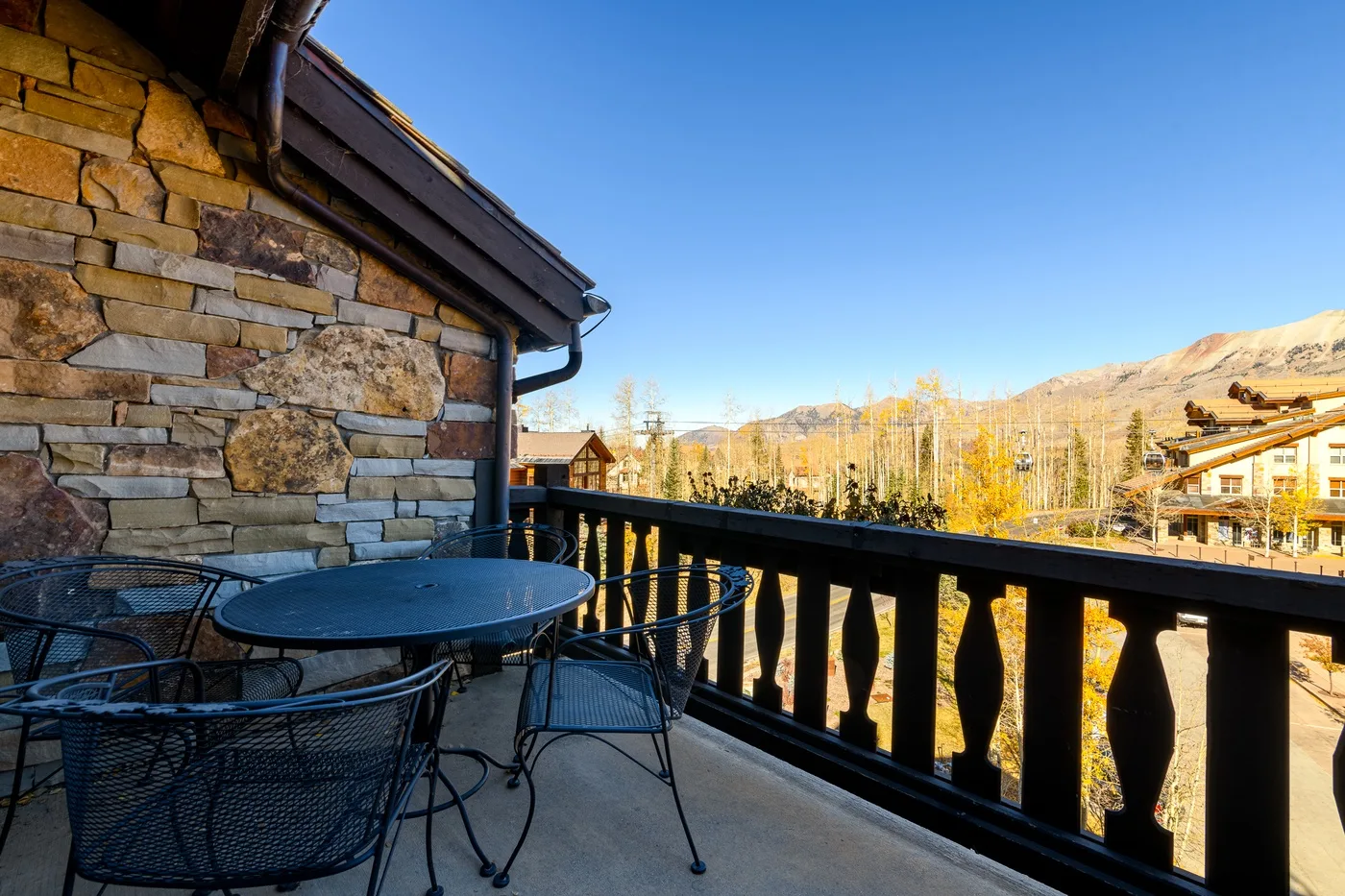 An outdoor balcony with a table and seating overlooks a mountain landscape.