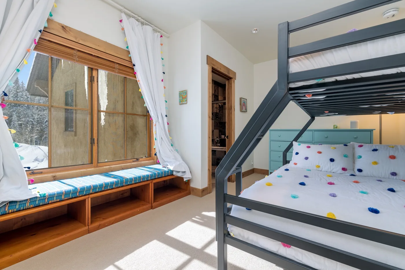 A bedroom with a dark bunk bed beside a large curtained window.