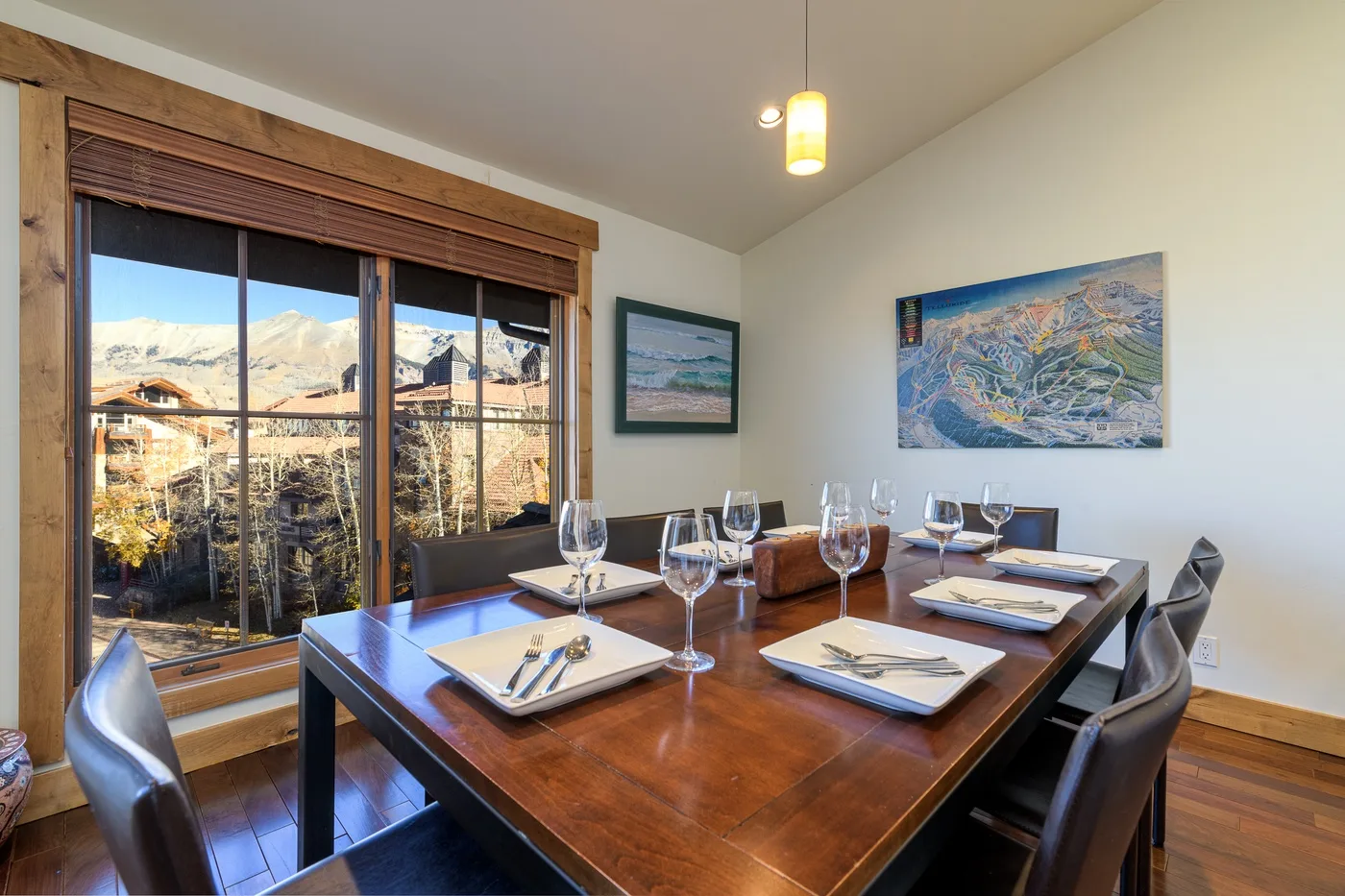 A dining room with a set table beside large windows overlooking a mountain landscape.