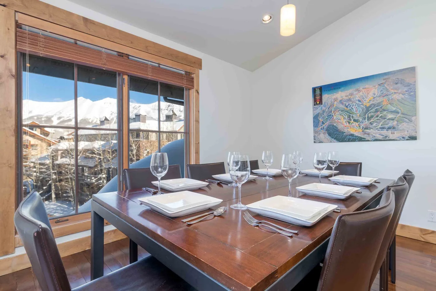 A dining area with a set table beside large windows overlooking a snowy landscape.