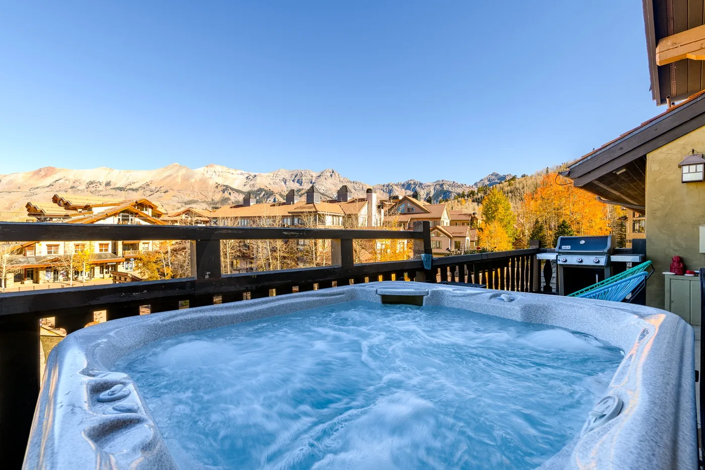A bubbling hot tub sits on a wooden deck with mountain views.