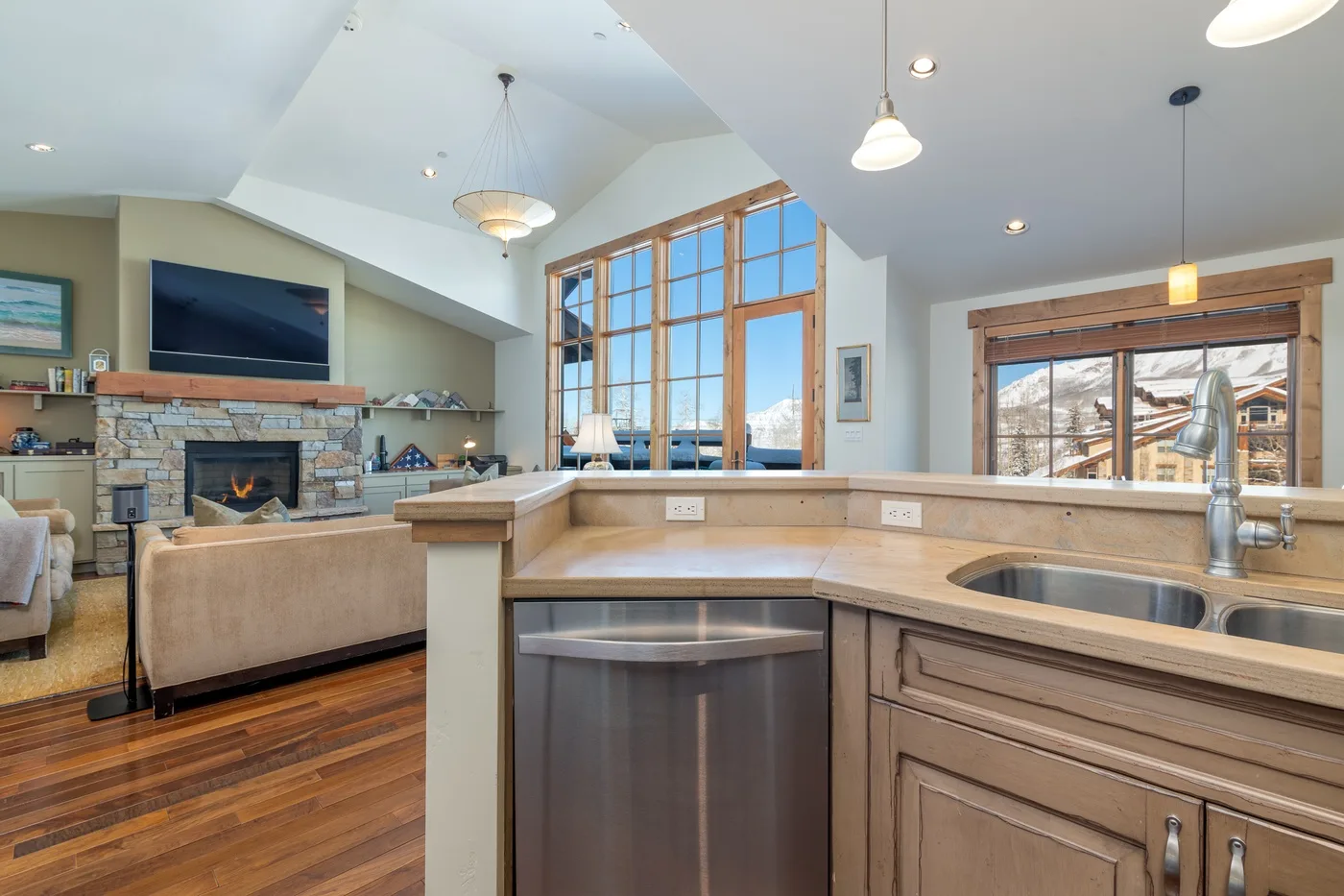An open kitchen with a counter and sink overlooks a living area with a fireplace.
