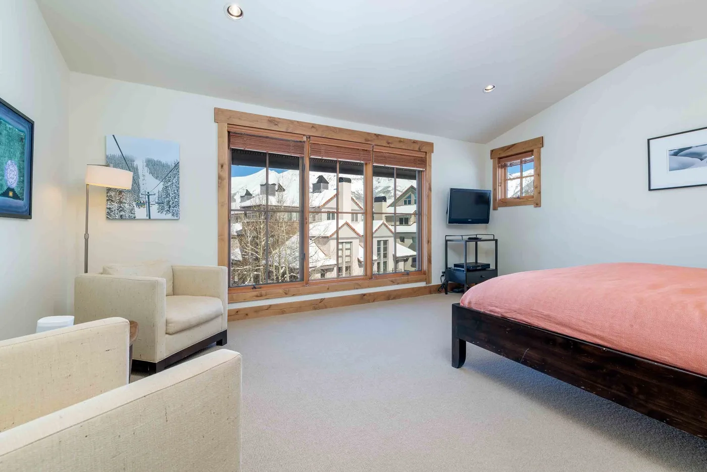 A bedroom with a bed, armchairs, and large windows overlooking nearby buildings.