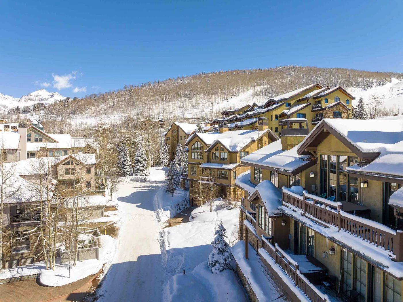 Snow-covered mountain buildings line a winter road beneath a clear blue sky.