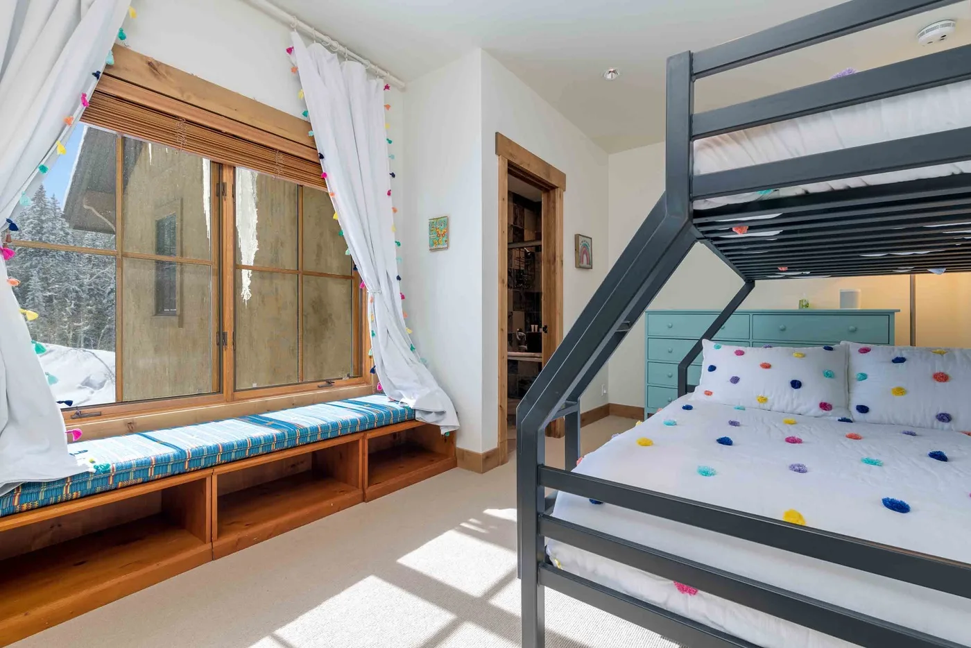 A bright bedroom with a bunk bed and a window seat beside the window.