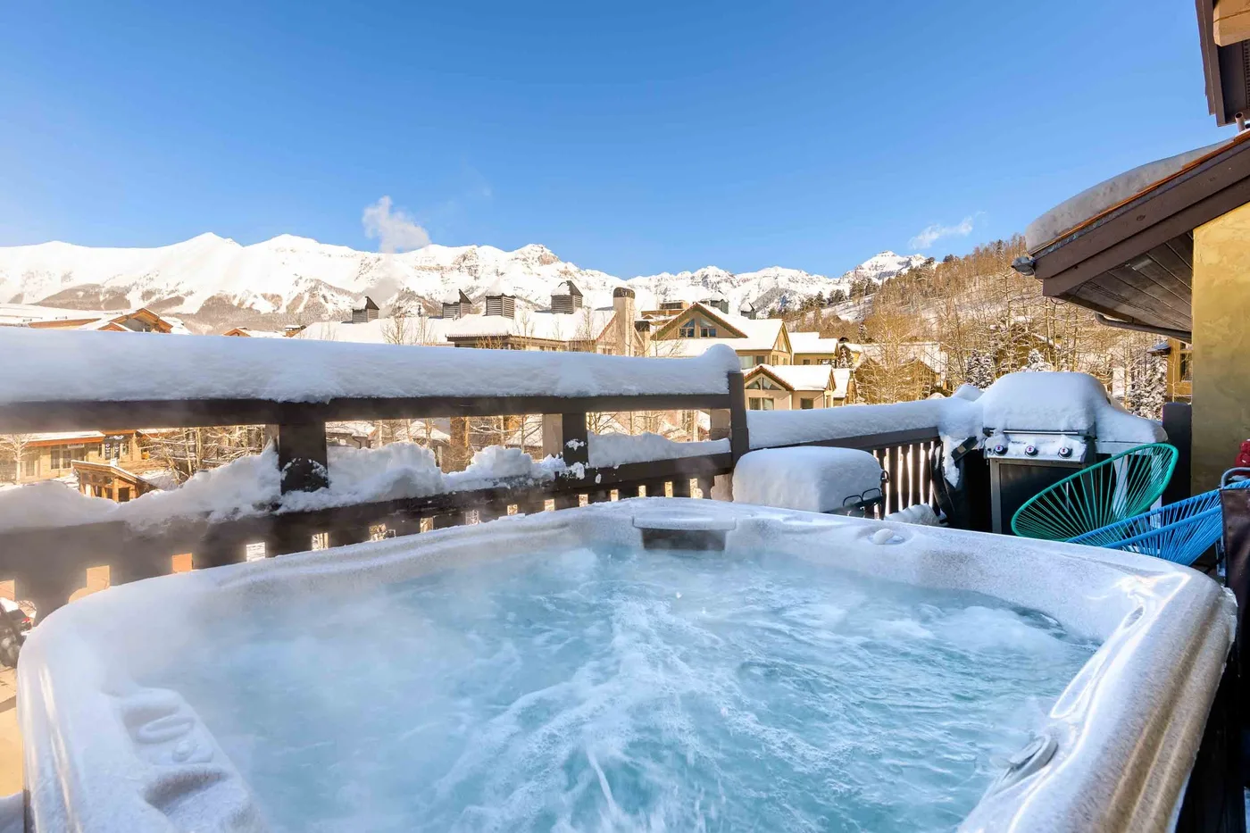 A bubbling hot tub sits on a snowy outdoor terrace with mountain views.
