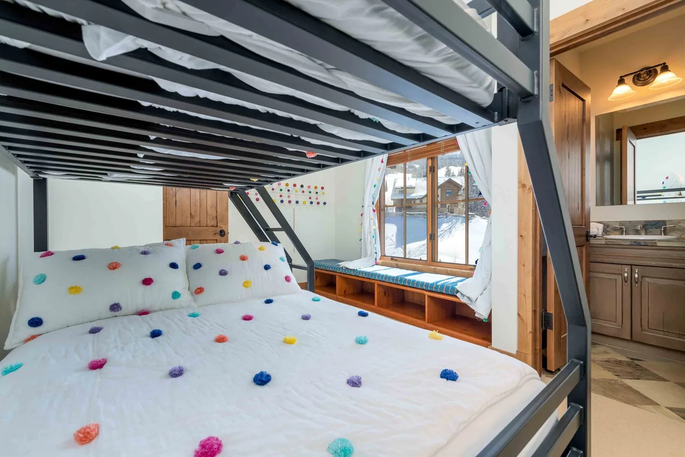 A bedroom with a bunk bed, colorful bedding, and a window beside the bed.