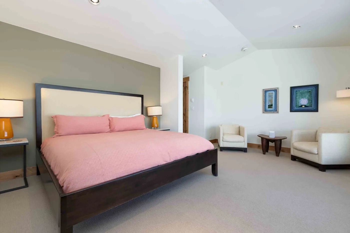 A bedroom with a large bed dressed in pink bedding and seating nearby.