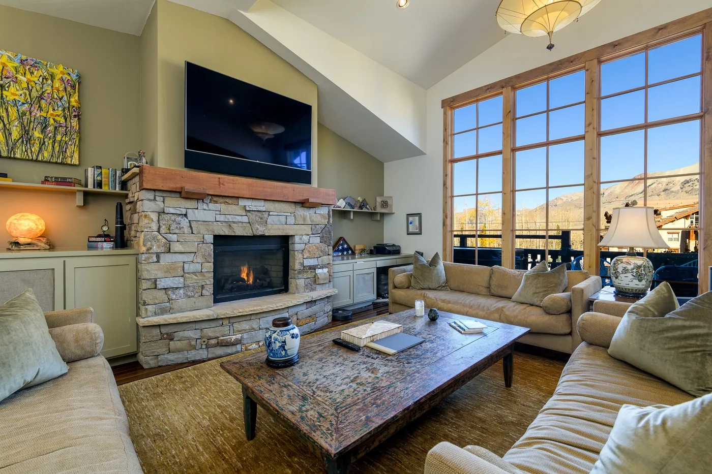 A living room with seating arranged around a stone fireplace and large windows.