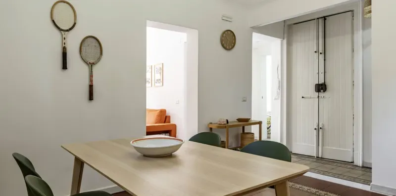 Comedor con una mesa rectangular, asientos y una puerta hacia una habitación contigua.