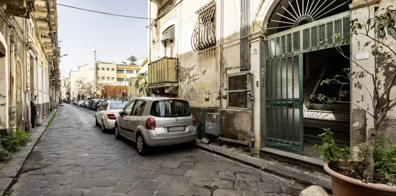 Una calle estrecha empedrada, bordeada de edificios y coches estacionados.