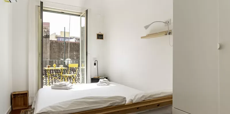 Un dormitorio luminoso con una cama blanca junto a una ventana abierta.