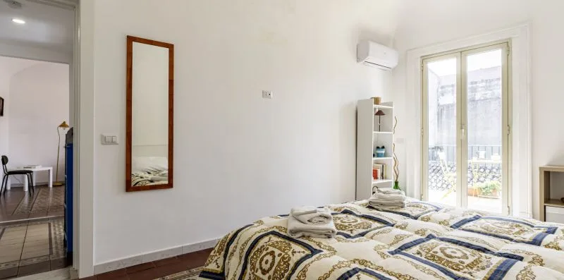 Un dormitorio con ropa de cama estampada y una puerta acristalada que da a un balcón.