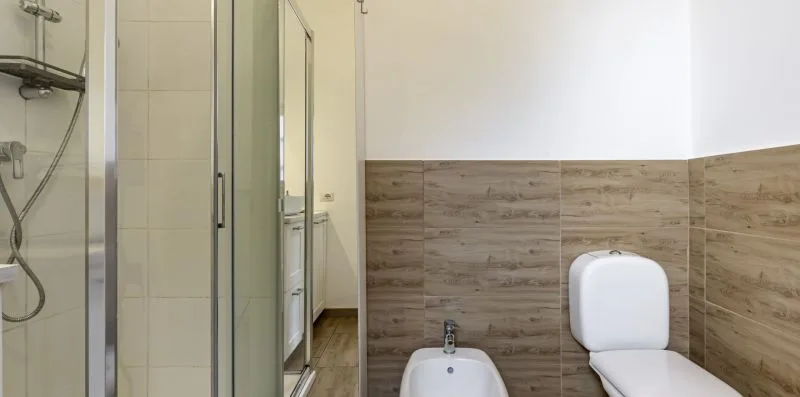 Un baño con mampara de ducha de vidrio, bidé e inodoro.