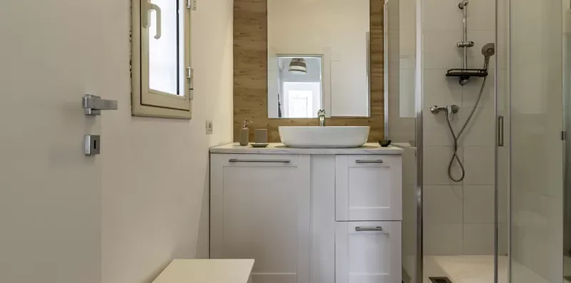 Un baño con lavabo, espejo de pared y ducha con panel de vidrio.