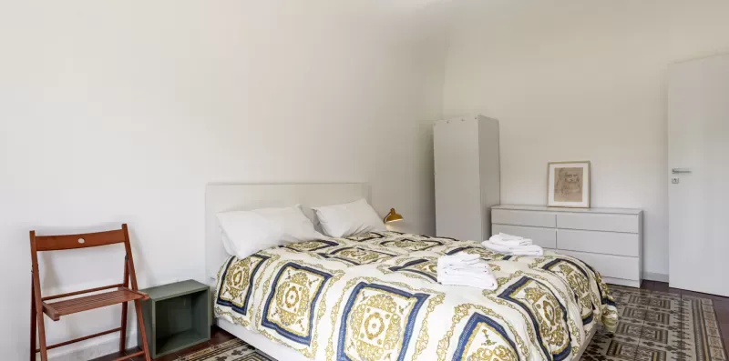 Un dormitorio con una colcha estampada y una silla de madera junto a la cama.