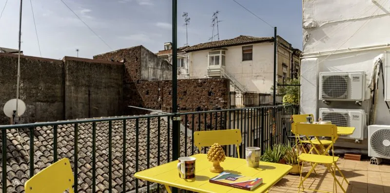 Un patio al aire libre con asientos amarillos y una mesa junto a una barandilla.