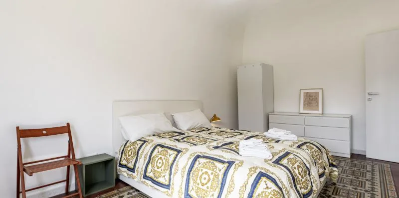 Dormitorio con una cama cubierta con una colcha estampada y una silla de madera cerca.