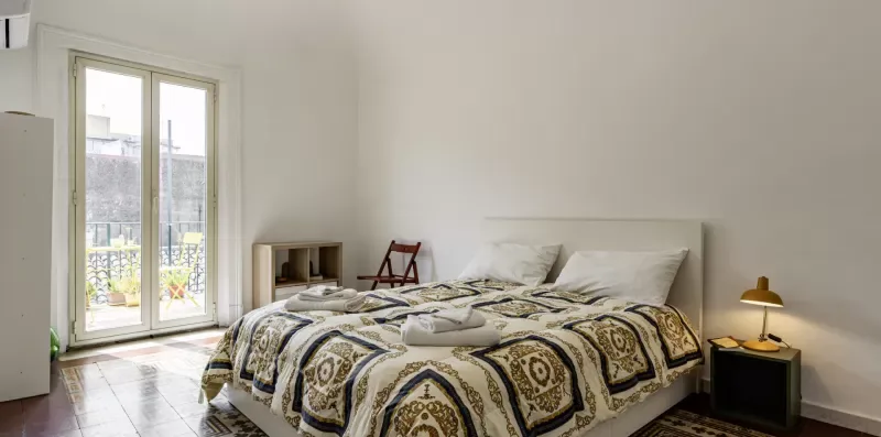 Un dormitorio con una cama cubierta por una colcha estampada junto a una ventana alta.