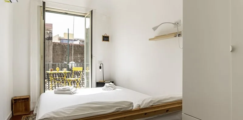 Un dormitorio con una cama junto a una ventana abierta que da a un balcón.