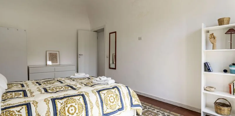 Un dormitorio con una colcha estampada y una estantería blanca.