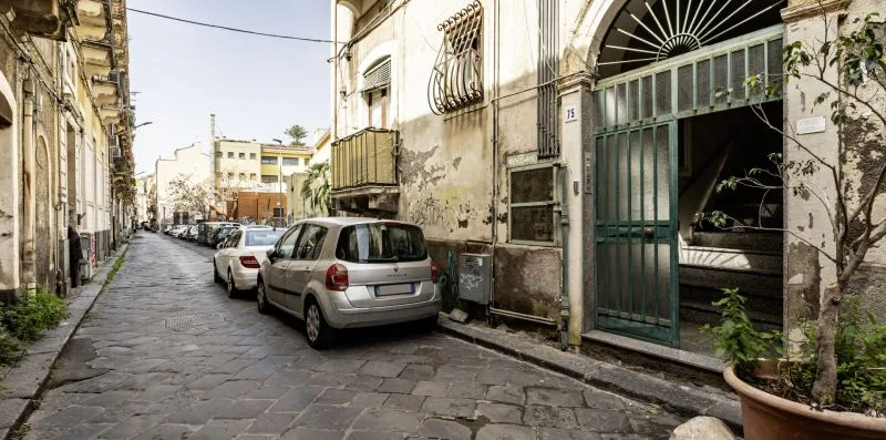 Una estrecha calle empedrada flanqueada por edificios antiguos y coches estacionados.