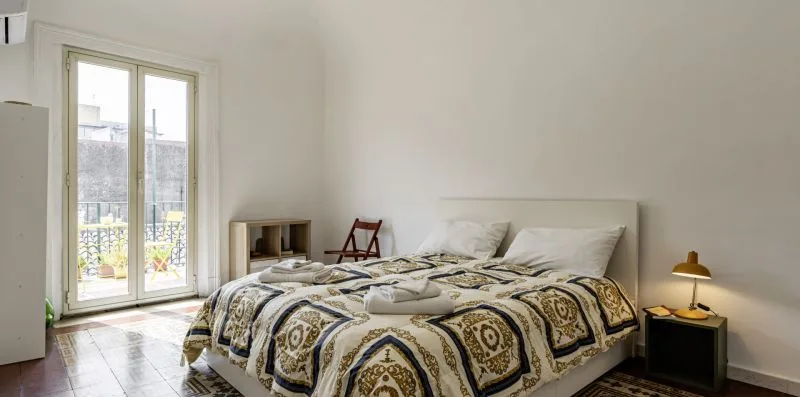 Dormitorio con una cama cubierta por una colcha estampada junto a una ventana alta.
