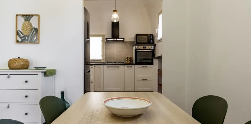 Una mesa de comedor con un cuenco mira hacia una cocina compacta con armarios blancos.