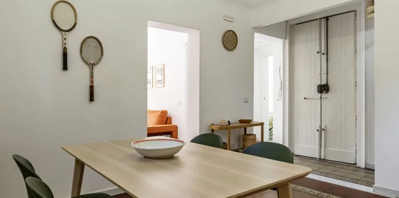 Comedor con una mesa de madera y sillas junto a una habitación contigua luminosa.