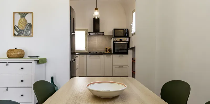 Una mesa de comedor queda frente a una cocina compacta con armarios y electrodomésticos.
