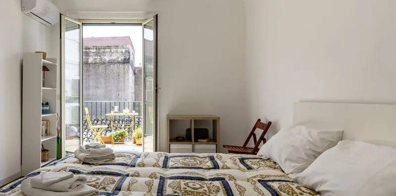 Un dormitorio con ropa de cama estampada y puertas abiertas que dan a un pequeño balcón.