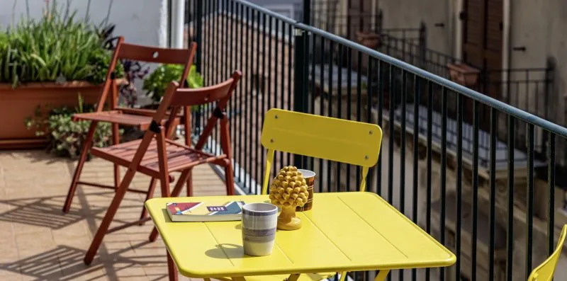 Una zona de estar en un balcón soleado con una mesa amarilla y sillas.