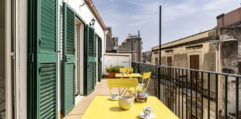 Una terraza en la azotea con una mesa amarilla y contraventanas verdes junto al edificio.