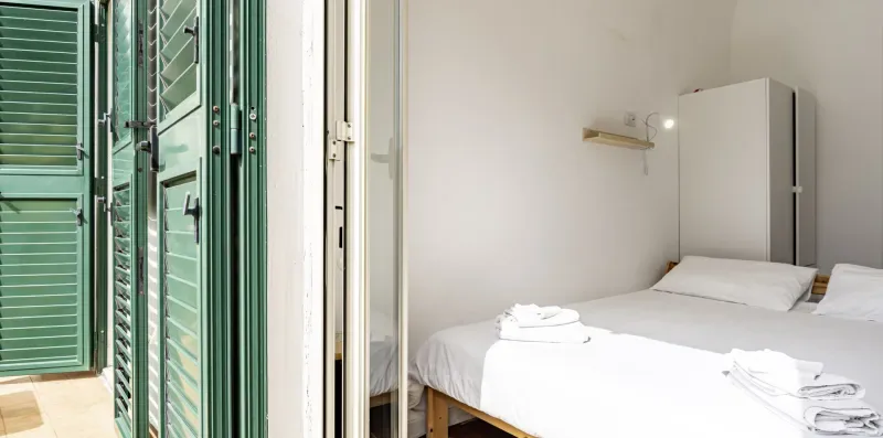Un dormitorio con ropa de cama blanca y persianas verdes junto a la cama.