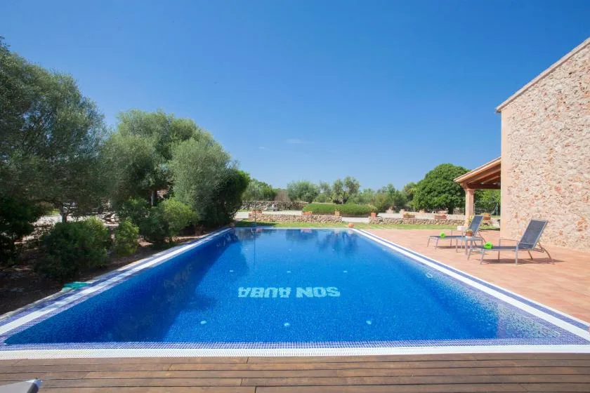 An outdoor swimming pool beside a stone building, with trees around the patio.