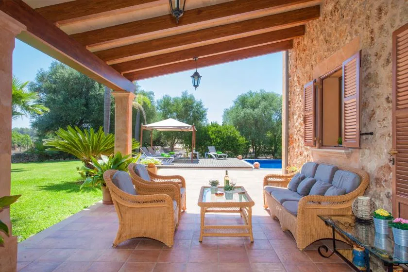 A covered patio with seating overlooks a garden and swimming pool.