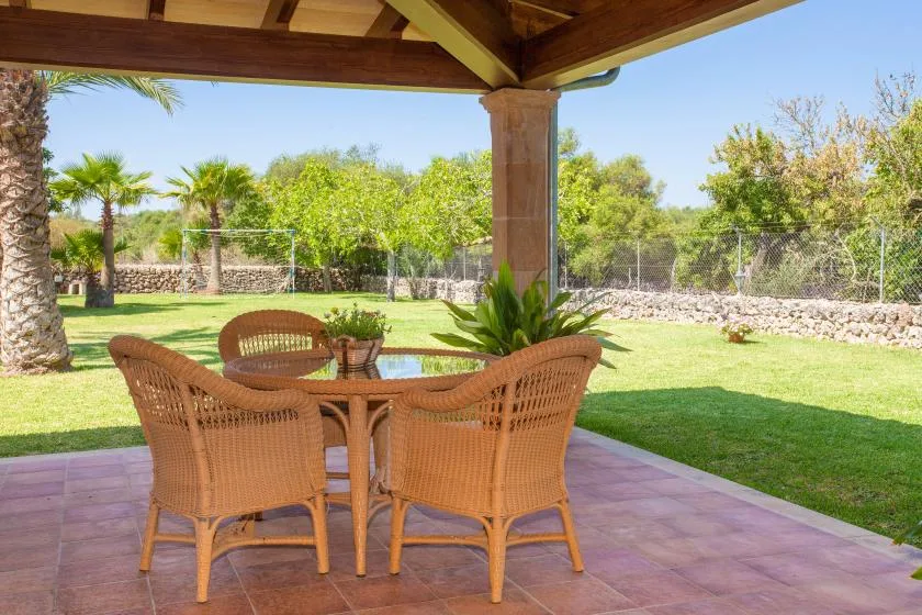 A covered patio has a wicker seating set around a glass-topped table.