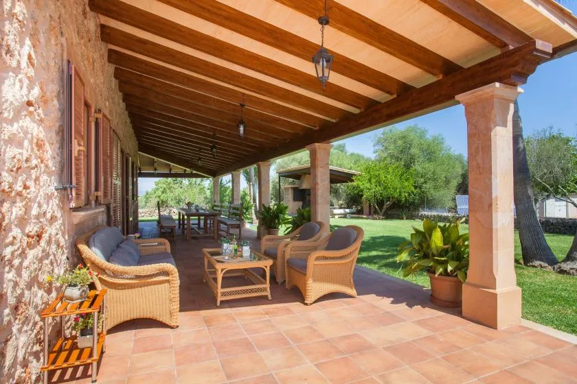 A covered patio with wicker seating overlooks a green garden.