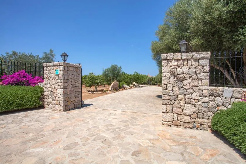 A paved stone driveway passes between stone pillars and landscaped greenery.